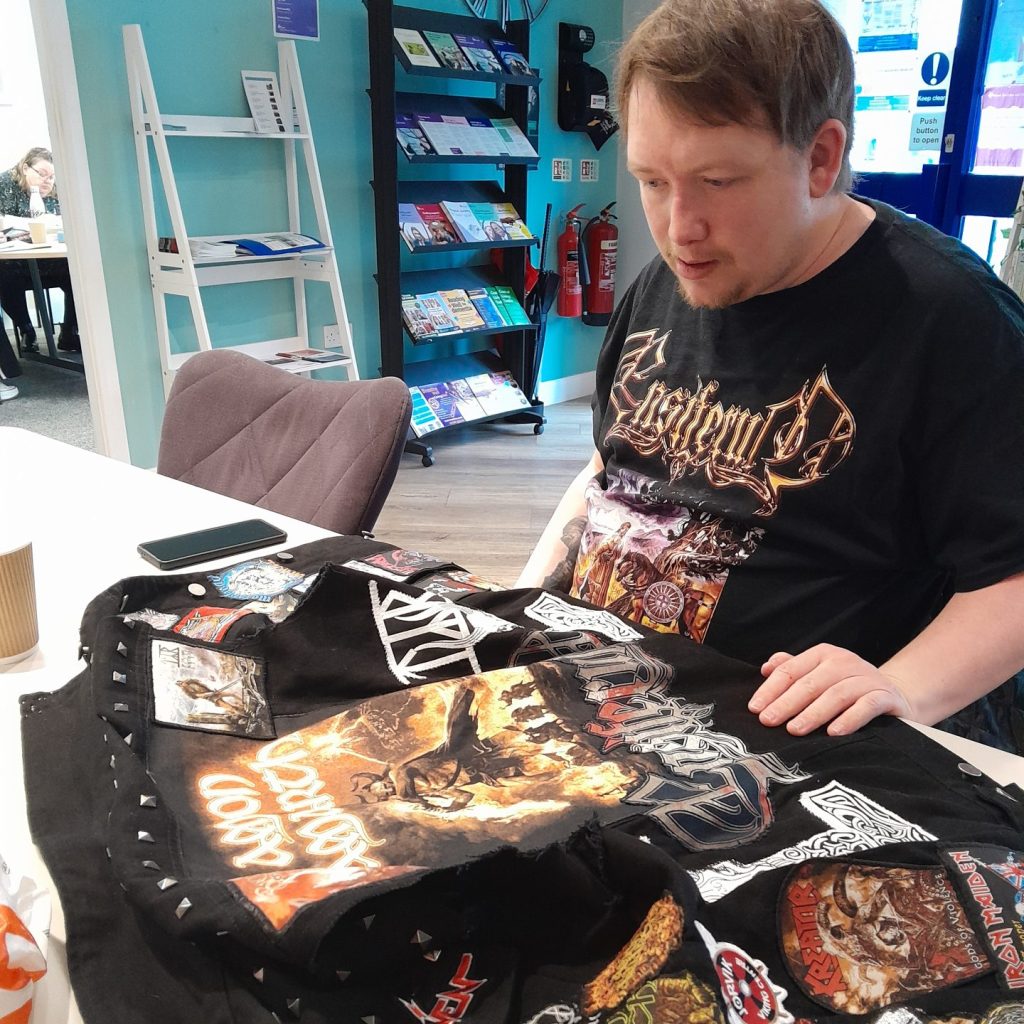 A man sits looking at a tshirt on the table in front of him after having added many badges to the shirt.